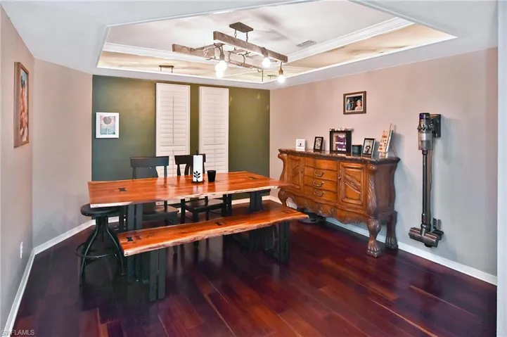 Dining room featuring a raised ceiling, dark wood-type flooring, and ornamental molding