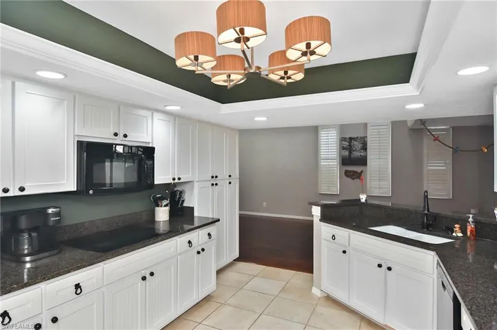 Kitchen with dark stone counters, white cabinets, black appliances, a raised ceiling, and crown molding