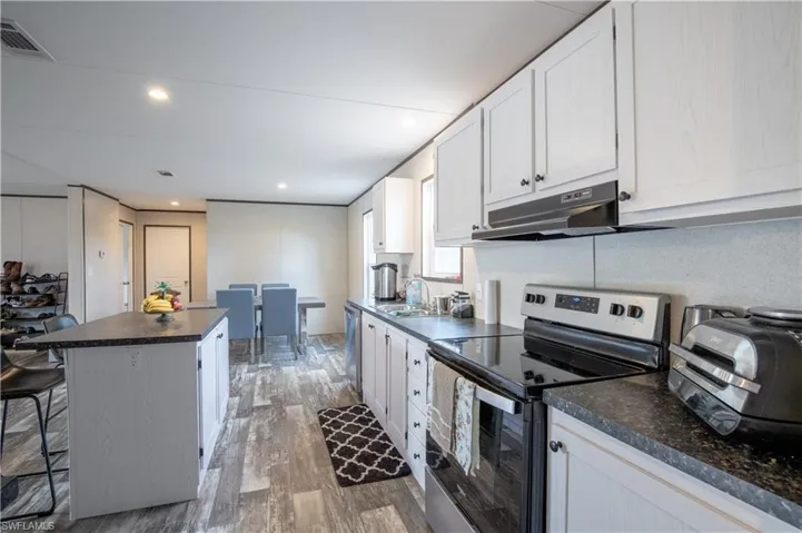 Kitchen featuring stainless steel appliances, dark hardwood / wood-style flooring, a kitchen island, and white cabinetry
