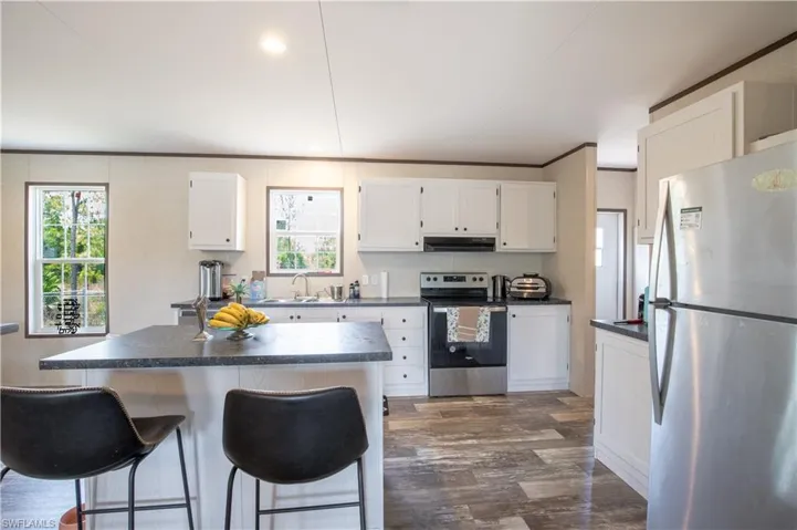 Kitchen featuring a center island, white cabinetry, stainless steel appliances, dark hardwood / wood-style floors, and a kitchen bar