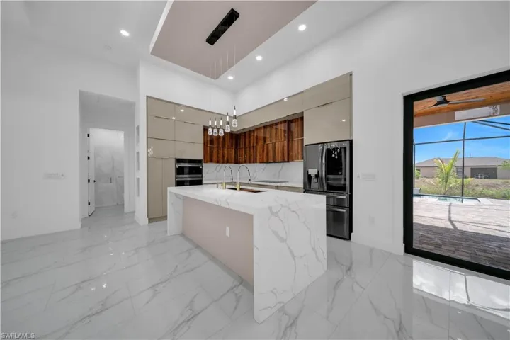 Kitchen featuring modern cabinets, stainless steel appliances, hanging light fixtures, a towering ceiling, and light stone countertops