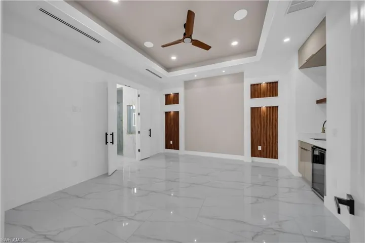 Unfurnished living room with a tray ceiling, light marble finish floors, recessed lighting, a ceiling fan, and beverage cooler