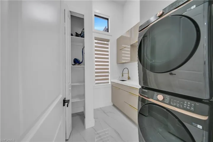 Laundry room with light marble finish floors, stacked washer / drying machine, and cabinet space
