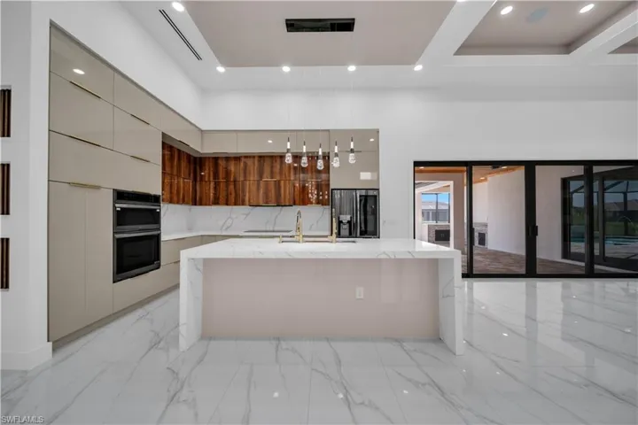 Kitchen with modern cabinets, a kitchen island with sink, recessed lighting, hanging light fixtures, and light stone counters