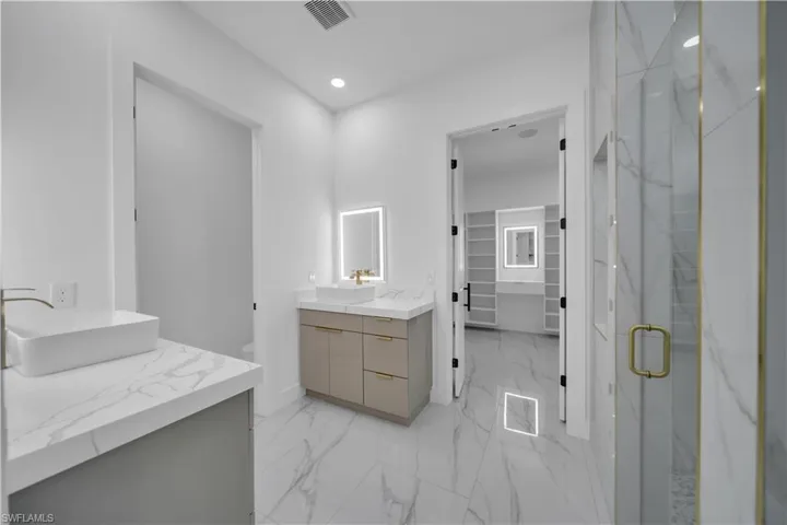 Bathroom featuring two vanities, a marble finish shower, a spacious closet, light marble finish floors, and recessed lighting