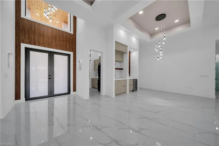 Entrance foyer featuring light marble finish floors, a high ceiling, a tray ceiling, french doors, and recessed lighting