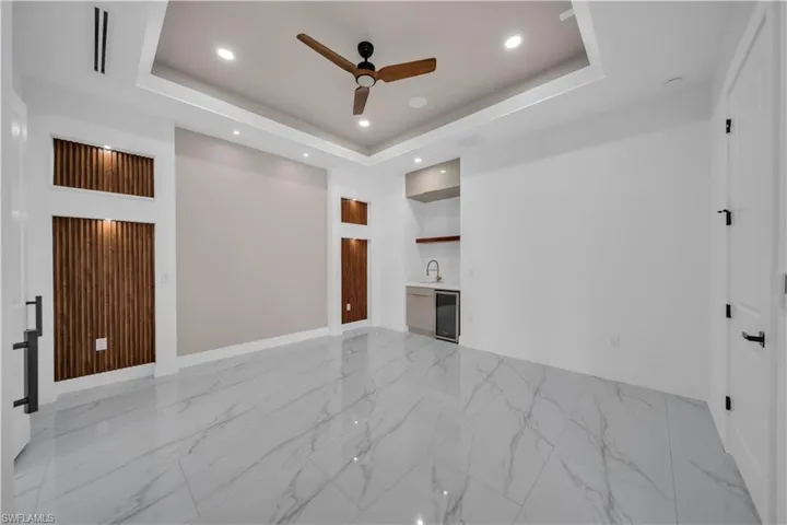 Unfurnished living room featuring a raised ceiling, a ceiling fan, recessed lighting, light marble finish flooring, and wine cooler