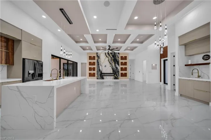 Kitchen featuring modern cabinets, light marble finish flooring, light stone countertops, fridge with ice dispenser, and pendant lighting
