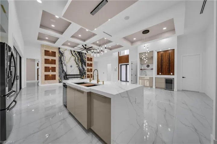 Kitchen with modern cabinets, a chandelier, freestanding refrigerator, coffered ceiling, and light marble finish floors