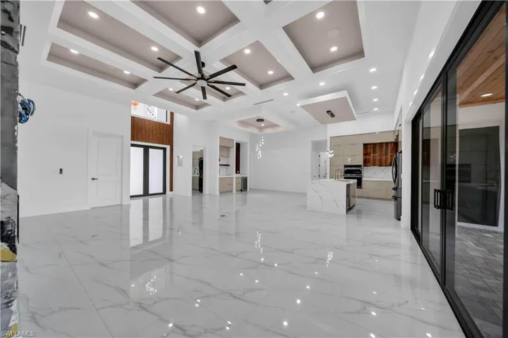 Unfurnished living room featuring light marble finish floors, coffered ceiling, a ceiling fan, beamed ceiling, and a high ceiling