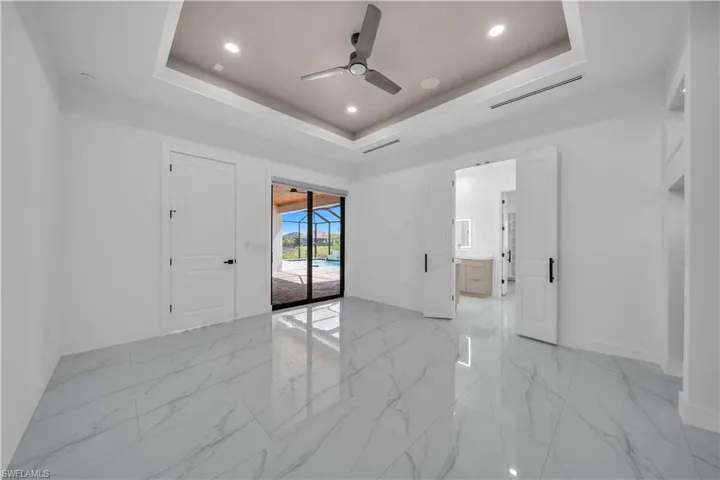 Empty room with a raised ceiling, a ceiling fan, recessed lighting, and light marble finish floors