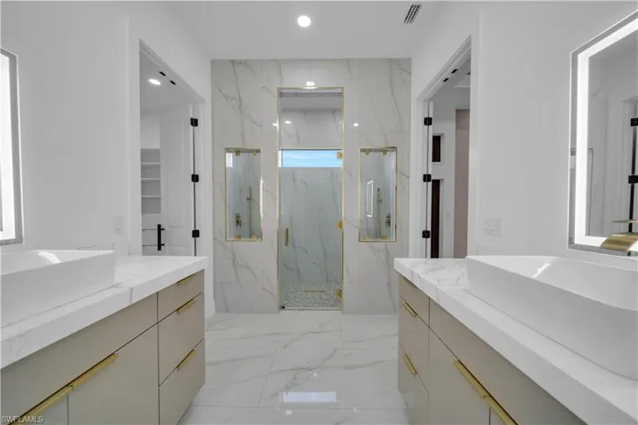 Full bath with two vanities, a marble finish shower, light marble finish floors, recessed lighting, and stone wall