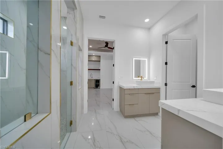 Bathroom featuring vanity, a marble finish shower, light marble finish flooring, recessed lighting, and wine cooler