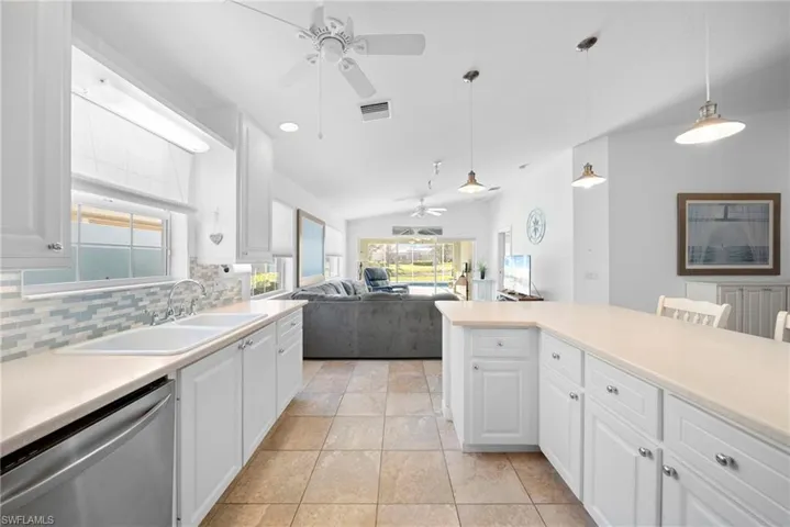 Kitchen featuring white cabinetry, light countertops, dishwasher, open floor plan, and vaulted ceiling