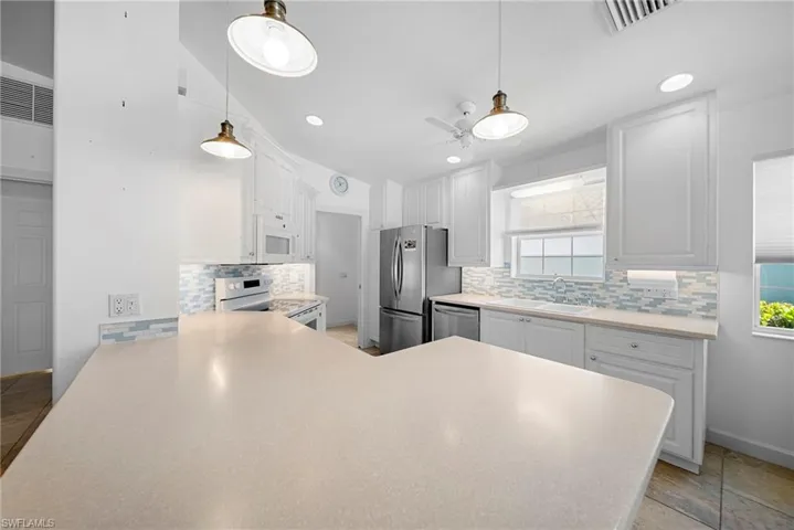 Kitchen with a peninsula, light countertops, white cabinets, white appliances, and pendant lighting