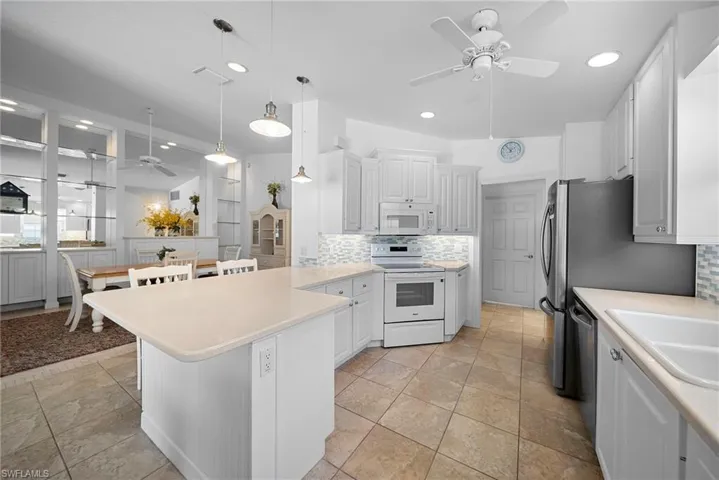 Kitchen with a ceiling fan, light countertops, white appliances, backsplash, and white cabinetry