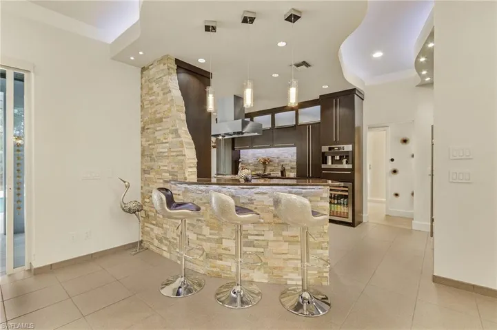 Bar featuring stainless steel oven, decorative light fixtures, island exhaust hood, tasteful backsplash, and dark brown cabinets. Monogram range, ovens, dishwasher and Miele built in coffee maker