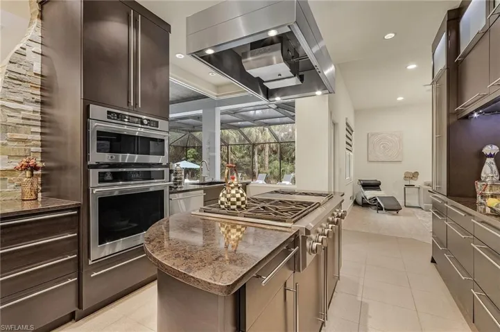 Kitchen with dark stone countertops, light tile patterned floors, range hood, a kitchen island, and Monogram appliances with stainless steel finishes. 6 bueners and griddle.