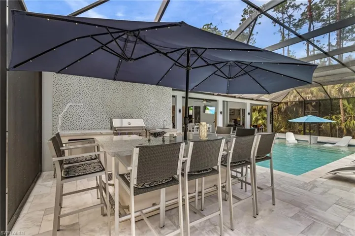 View of swimming pool with a patio, exterior bar, grilling area, exterior kitchen, and glass enclosure