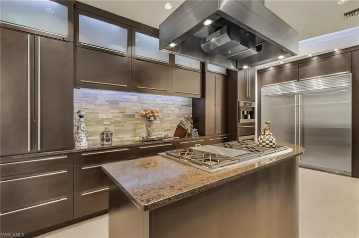 Kitchen featuring stainless steel appliances, tasteful backsplash, stone countertops, a kitchen island, and island range hood. the largest Sub-Zero refrigerator and freeaer perfect for entertaining.