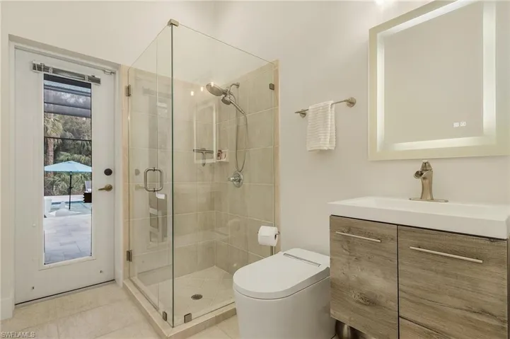 Bathroom with smart toilet, floating vanity, tile patterned flooring, and a frameless shower with shower door