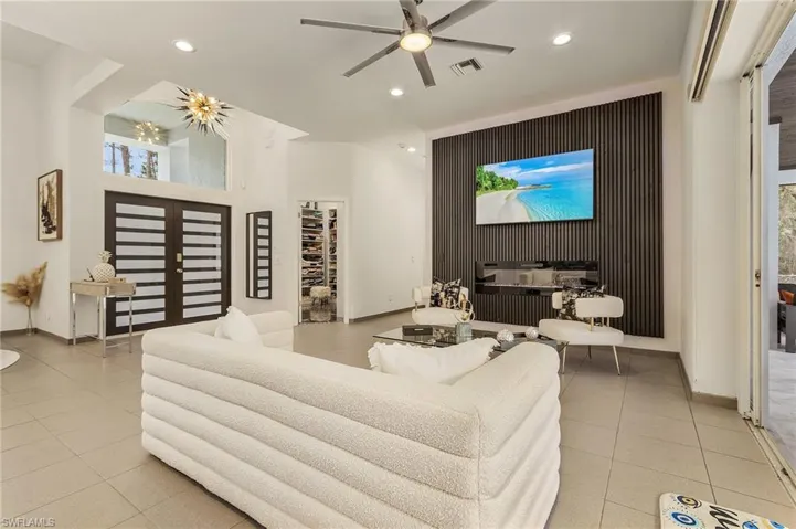 Tiled living room featuring ceiling fan with notable chandelier and impact windows and doors