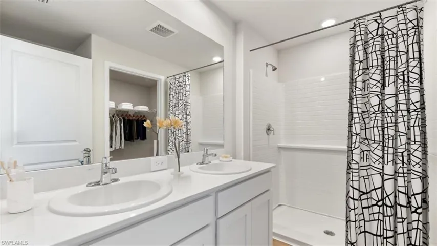 This image is virtually staged. Full bathroom featuring double vanity, a stall shower, a walk in closet, and recessed lighting