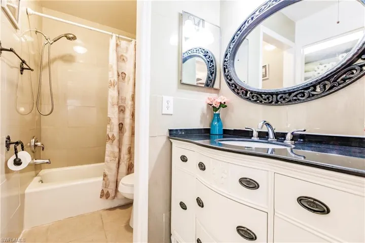 Bathroom featuring a white vanity with a dark countertop, an ornate oval mirror, and a built-in bathtub with shower
