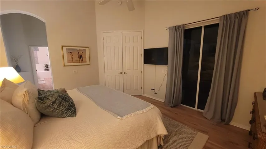 Bedroom with wood finished floors, a closet, a high ceiling, arched walkways, and a ceiling fan