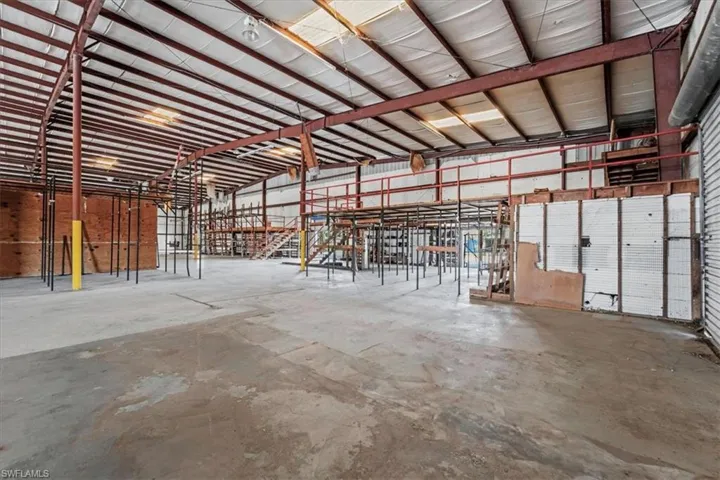 Spacious commercial interior featuring concrete flooring, exposed structural steel beams, high ceilings, and an elevated mezzanine
