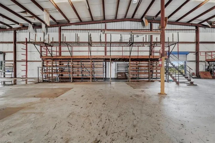 Expansive warehouse space featuring concrete flooring, exposed structural steel beams, a metal roof with skylights, and a built-in mezzanine structure with access stairs