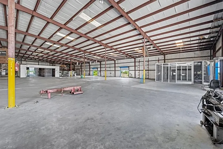 Spacious industrial interior featuring a high metal truss ceiling, exposed structural beams, and concrete flooring