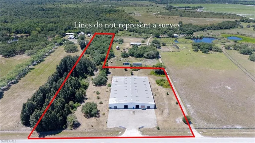 Expansive rural property featuring a large commercial-style building with multiple bays, extensive paved and unpaved areas, and mature tree lines