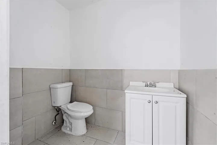 Bathroom featuring a white toilet, floor-to-ceiling gray wall tiling, a white vanity with integrated sink, and chrome faucet fixtures
