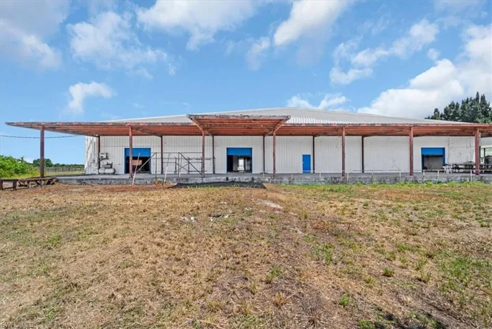 Industrial building featuring a white corrugated metal exterior, multiple blue roll-up doors, an extended covered loading dock, and a metal roof
