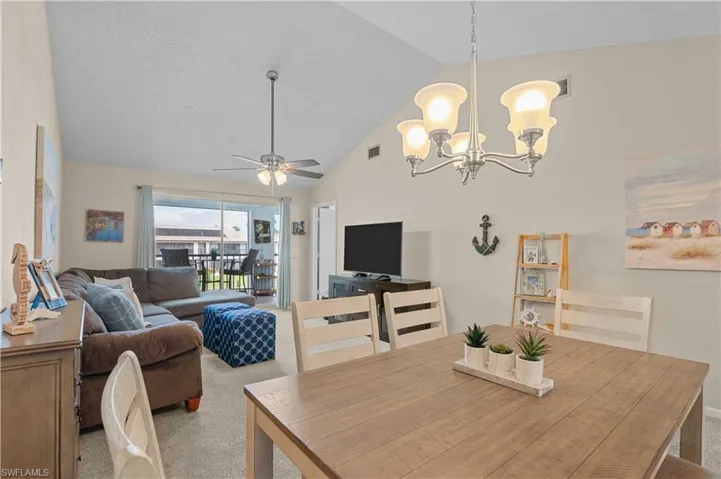 Dining space featuring carpet floors, a chandelier, a ceiling fan, and high vaulted ceiling