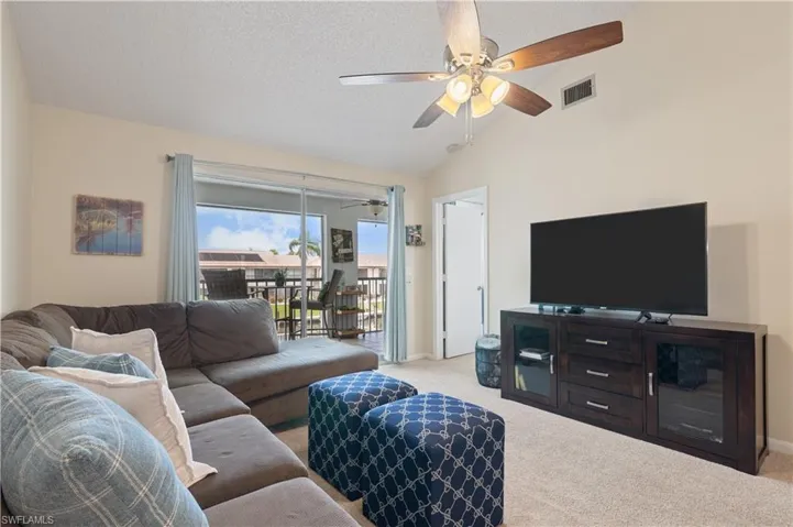 Living area featuring light carpet, lofted ceiling, a textured ceiling, and a ceiling fan