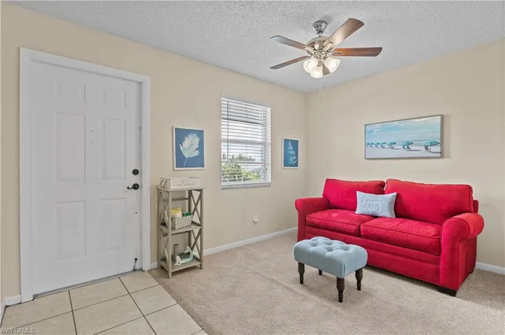 Living area with light colored carpet, a textured ceiling, light tile patterned floors, and a ceiling fan
