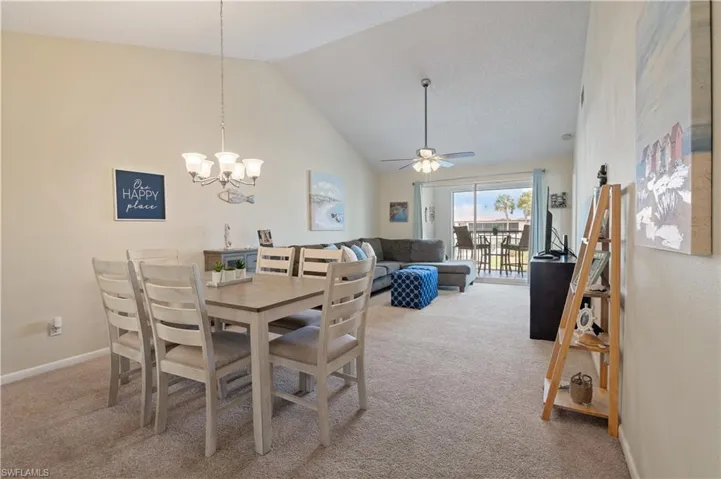Dining room featuring high vaulted ceiling, light colored carpet, ceiling fan, and a chandelier