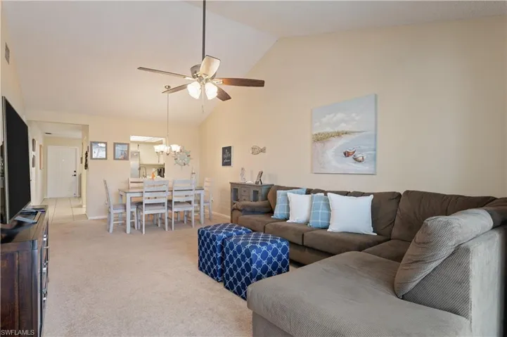 Living room with carpet floors, ceiling fan, high vaulted ceiling, and a chandelier