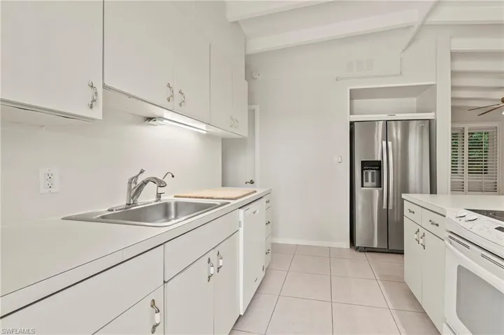 Kitchen with white appliances, light countertops, visible vents, beam ceiling, and a sink
