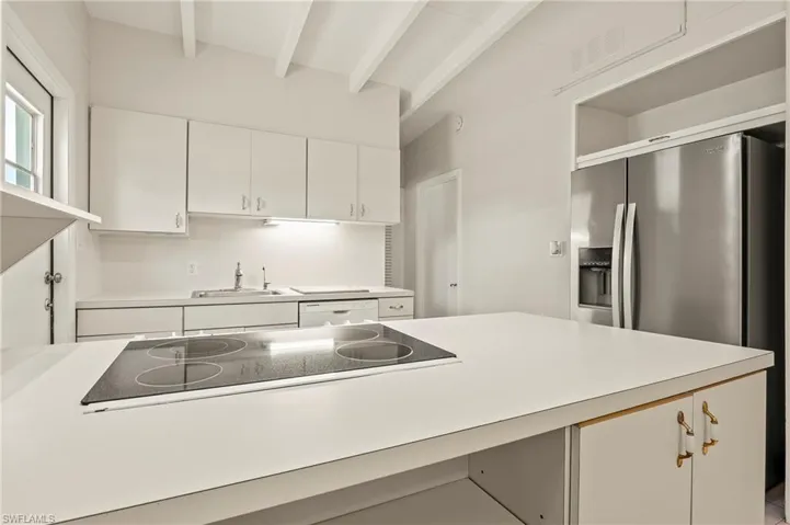 Kitchen featuring beamed ceiling, stainless steel fridge with ice dispenser, white cabinetry, a sink, and black electric cooktop