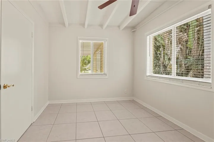Bedroom with light tile patterned flooring, beamed ceiling, baseboards, and a ceiling fan