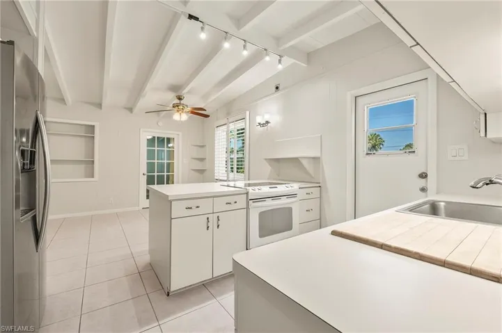 Kitchen with beamed ceiling, a peninsula, a sink, stainless steel fridge, and white electric stove