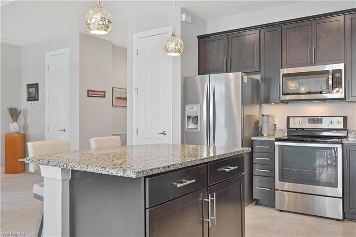 Kitchen with pendant lighting, light tile patterned floors, stainless steel appliances, and dark brown cabinets