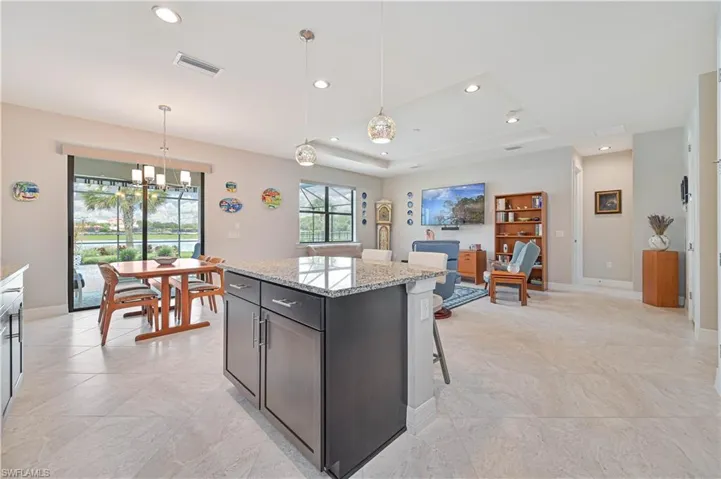 Kitchen with an inviting chandelier, light stone countertops, a center island, a tray ceiling, and light tile patterned flooring