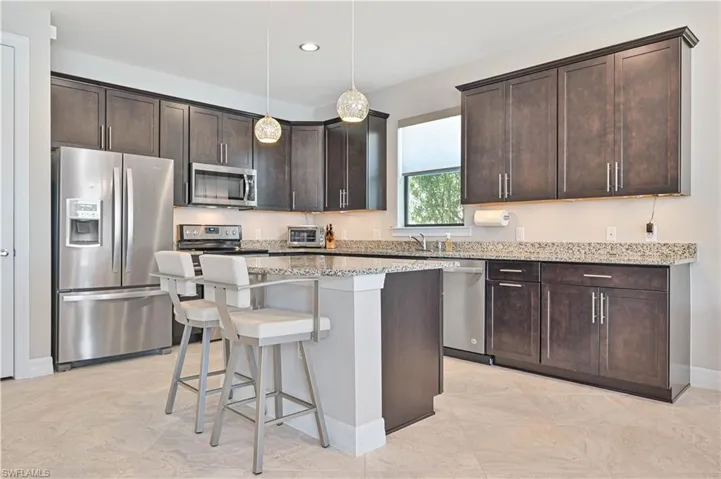 Kitchen with appliances with stainless steel finishes, light stone counters, light tile patterned flooring, and a kitchen island