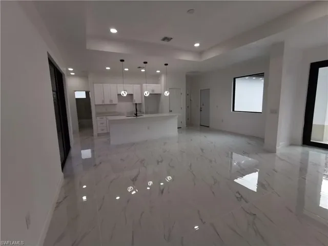 Unfurnished living room with a tray ceiling, recessed lighting, and light marble finish flooring