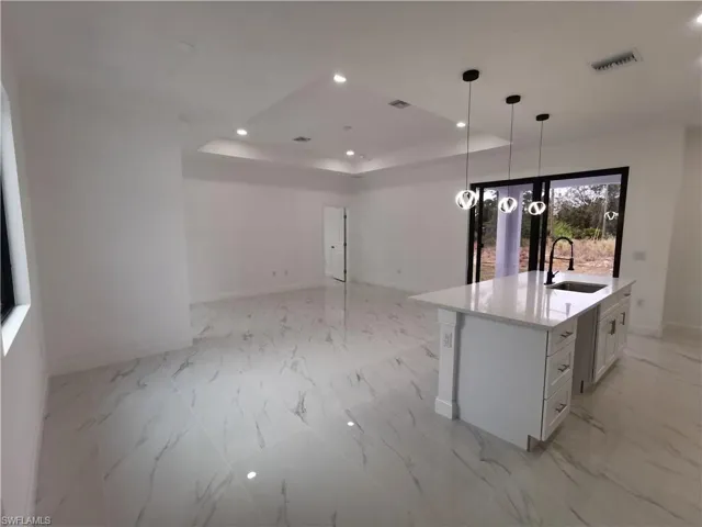 Kitchen featuring a raised ceiling, light stone countertops, decorative light fixtures, recessed lighting, and white cabinetry