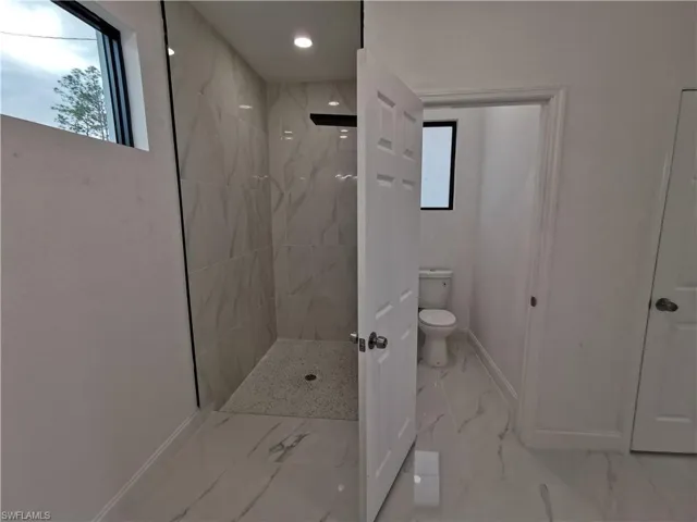 Full bath featuring a marble finish shower and light marble finish flooring